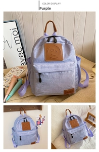 Detail of purple canvas backpack showing brown leather smiley face patch and high-quality texture