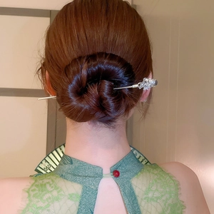 Detail of silver hair pin with floral carving and pearl accent on a braided bun hairstyle