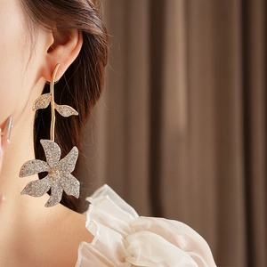 Close-up of model wearing gold flower earrings with crystals in a leaf design