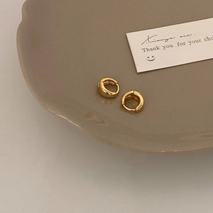 Macro detail of polished gold hoop earrings on a beige ceramic plate with high gloss finish