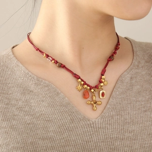 Detail of red braided cord necklace featuring golden cross pendant and tiger eye beads