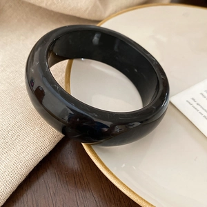 Close-up of a wide polished black resin bangle on a decorative white porcelain plate