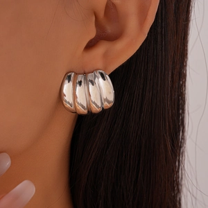 Macro shot of silver textured shell style earrings with vertical folds on a model