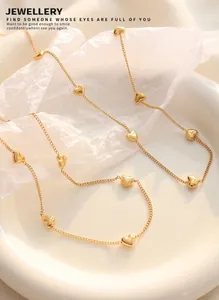 Gros plan d'un collier en acier titane doré avec petits pendentifs en cœur sur céramique