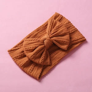 Macro detail of caramel cable knit baby headband featuring a large soft bow design
