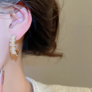 Detail of C-shaped gold-plated earring with zircons and pearls on female model