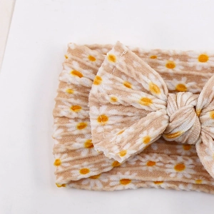 Close-up of beige corduroy baby headband featuring yellow daisy patterns and a soft bow