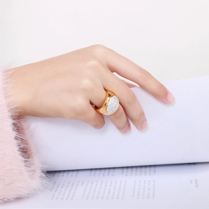 Detail of a large gold oval ring fully set with white crystals worn by a model