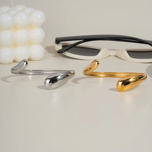 Detail of wave-shaped open bangles in gold and silver finish with teardrop ends
