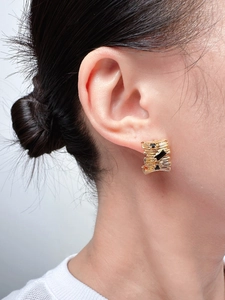 Macro shot of gold textured C-shape earring with black zircon stone on model