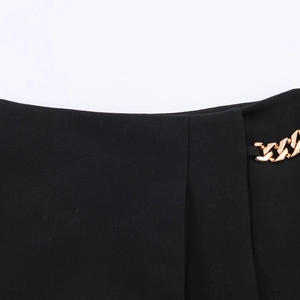 Detailaufnahme der Goldkette und Plissee-Stofftextur an der schwarzen Shorts