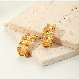 Macro shot of 18K gold-plated irregular wavy earrings on beige travertine stone display