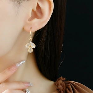 Close-up of golden teardrop earring with opal stone and crystal flower detail on model