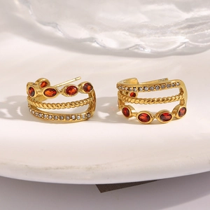Detailed macro view of 18K gold-plated C-shaped earrings with red zircon and crystal stones