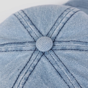 Top detail of blue denim baseball cap featuring six-panel stitching and central button