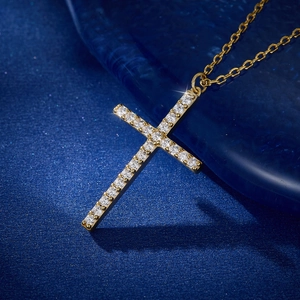 Macro shot of gold cross pendant with cubic zirconia stones on dark blue background