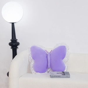 Detail of purple butterfly plush pillow with white lace trim on a minimalist white sofa