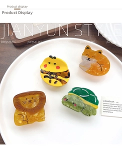 Flat lay of colorful acetate hair claws in lion, cat, bee, and turtle shapes on a tray