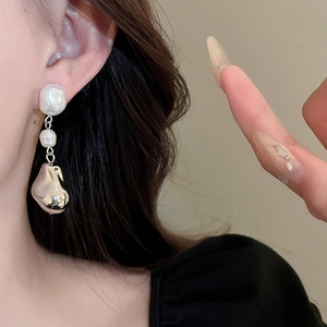 Gros plan sur des boucles d'oreilles en perles baroques et pendentifs métalliques