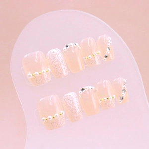 Pink press-on nails with pearls and glitter details on a frosted display board