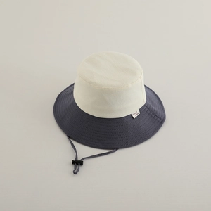 Detail of color-block sun hat showing beige crown, navy brim, and adjustable wind rope