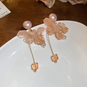 Dettaglio di orecchini a fiore rosa con perle e nappe su un piatto di ceramica bianca