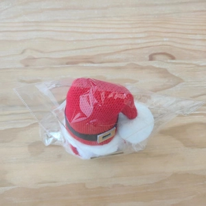 Detail view of a red knitted Christmas hat for pets with black belt on a wooden surface