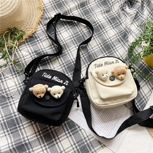 Detail of canvas crossbody bags in black and beige with cute bear decor and lettering
