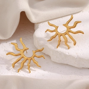 Detailed view of sunburst gold earrings placed on white textured stone and soft fabric
