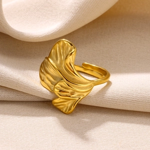 Macro detail of golden ginkgo leaf ring with adjustable band on warm fabric background