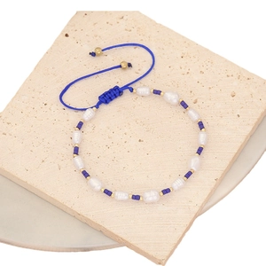 Handmade pearl bead bracelet with blue woven cord on a textured stone surface