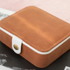 Portable brown suede jewelry box with white trim and golden metal snap fastener