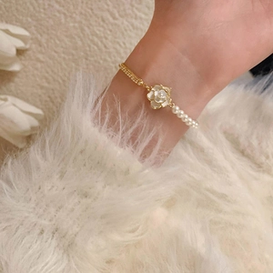 Detailed view of camellia pearl bracelet featuring a gold chain on woman's wrist