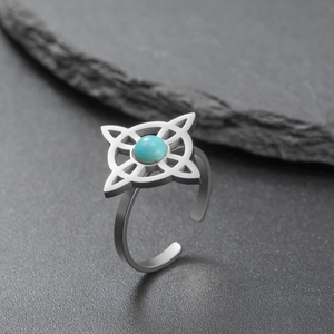 Macro shot of silver stainless steel witch knot ring with turquoise stone on dark stone