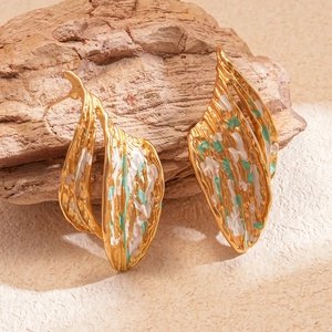 Detail of gold wrinkled leaf earrings with white and green enamel on a natural rock
