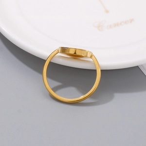 Minimalist gold stainless steel ring with flat circular setting on a white ceramic plate