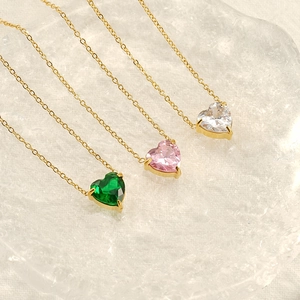 Close-up of three gold heart-shaped zircon necklaces in emerald, pink and white stones