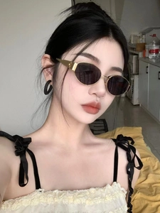 Close-up of retro oval sunglasses with gold metal frames and dark lenses on a model