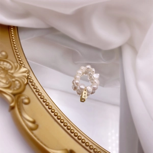 Detail of freshwater pearl ring with a gold letter B pendant on a vintage mirror