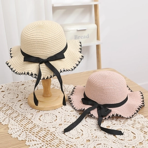 Close-up of woven sun hats with black bow ribbons and decorative stitched edges