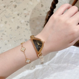 Détail d'une montre dorée triangulaire de luxe et d'un bracelet trèfle au poignet