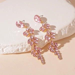 Detailed shot of pink crystal leaf earrings with gold tassels on stone pedestal