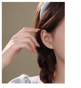 Detail of s925 silver blue butterfly and flower stud earrings worn on a model's ear