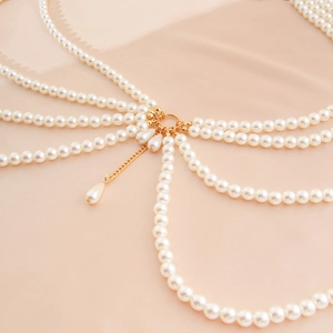 Detail of layered pearl body chain with golden rings and teardrop pendants on silk