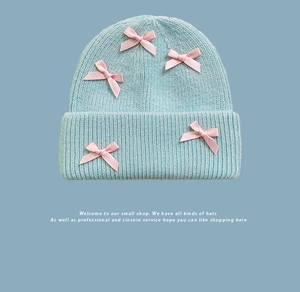 Dettaglio del berretto in maglia azzurro con decorazioni di fiocchi in nastro di raso rosa
