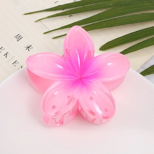 Macro detail of a pink gradient acrylic frangipani flower hair claw on a white plate