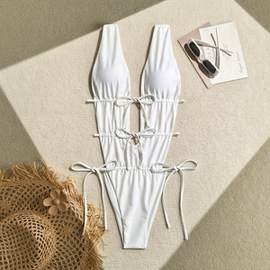 Flat lay of white one-piece swimsuit with plunging neckline and side cut-outs on sand mat