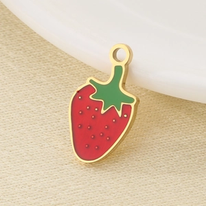 Macro shot of red and green enamel strawberry charm with gold metal edges on fabric