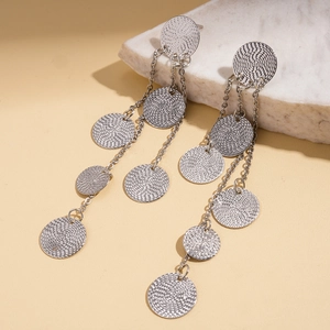 Detail of silver long tassel earrings with textured round metal discs on marble
