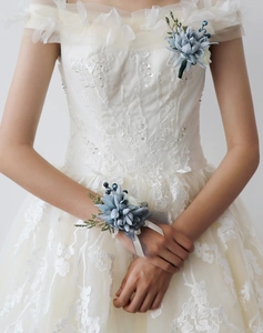 Détail de la boutonnière et du bracelet de fleurs bleu Morandi sur dentelle